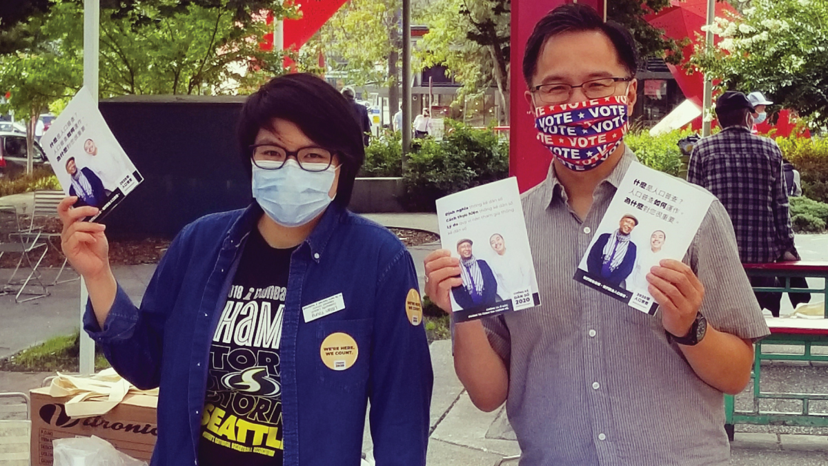 two people in masks holding up census information at outside table