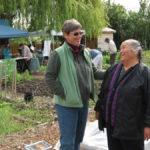 two people in jackets standing in garden, smiling at each other
