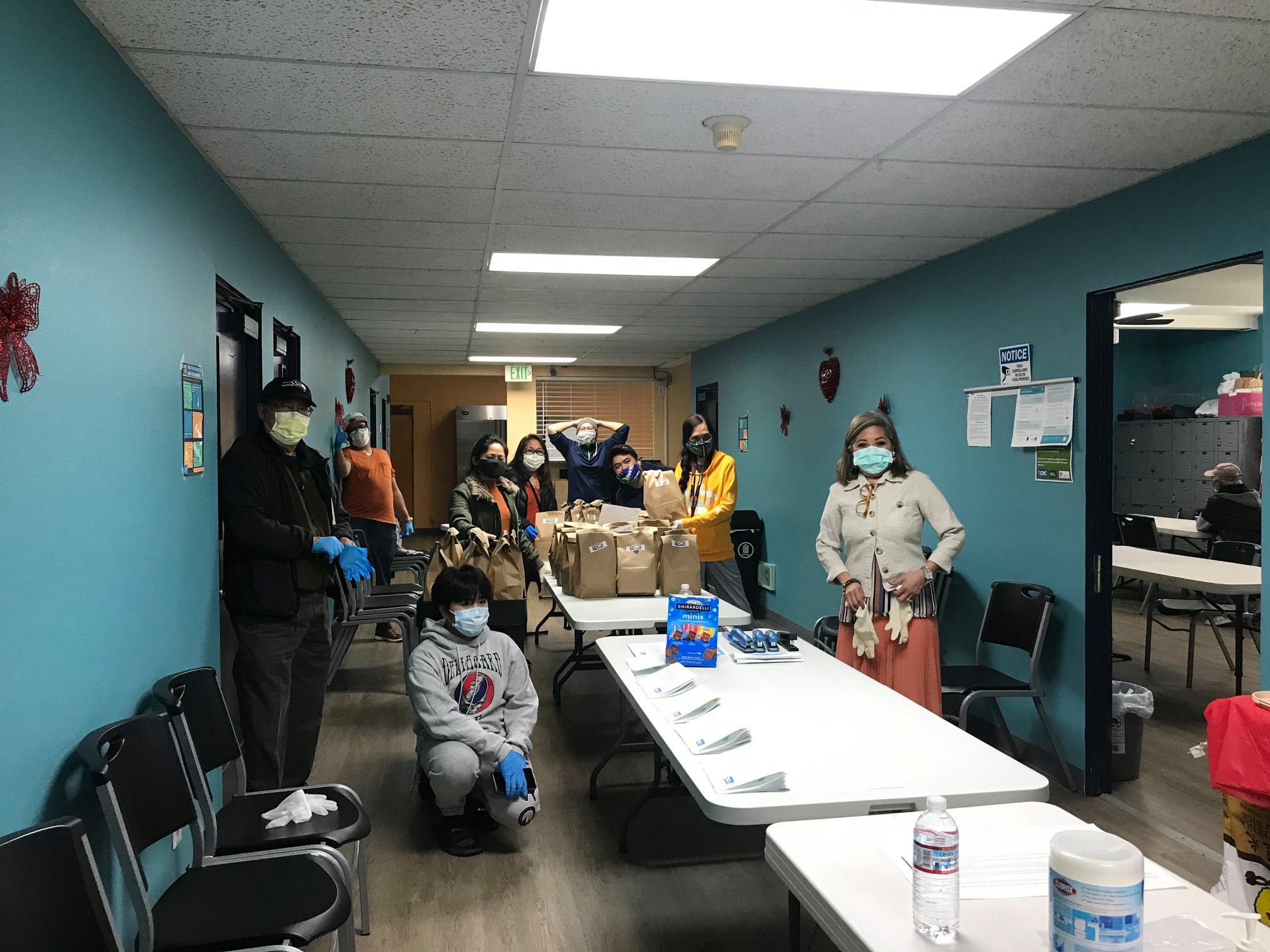 masked volunteers assembling bagged meals on tables in a long hallway