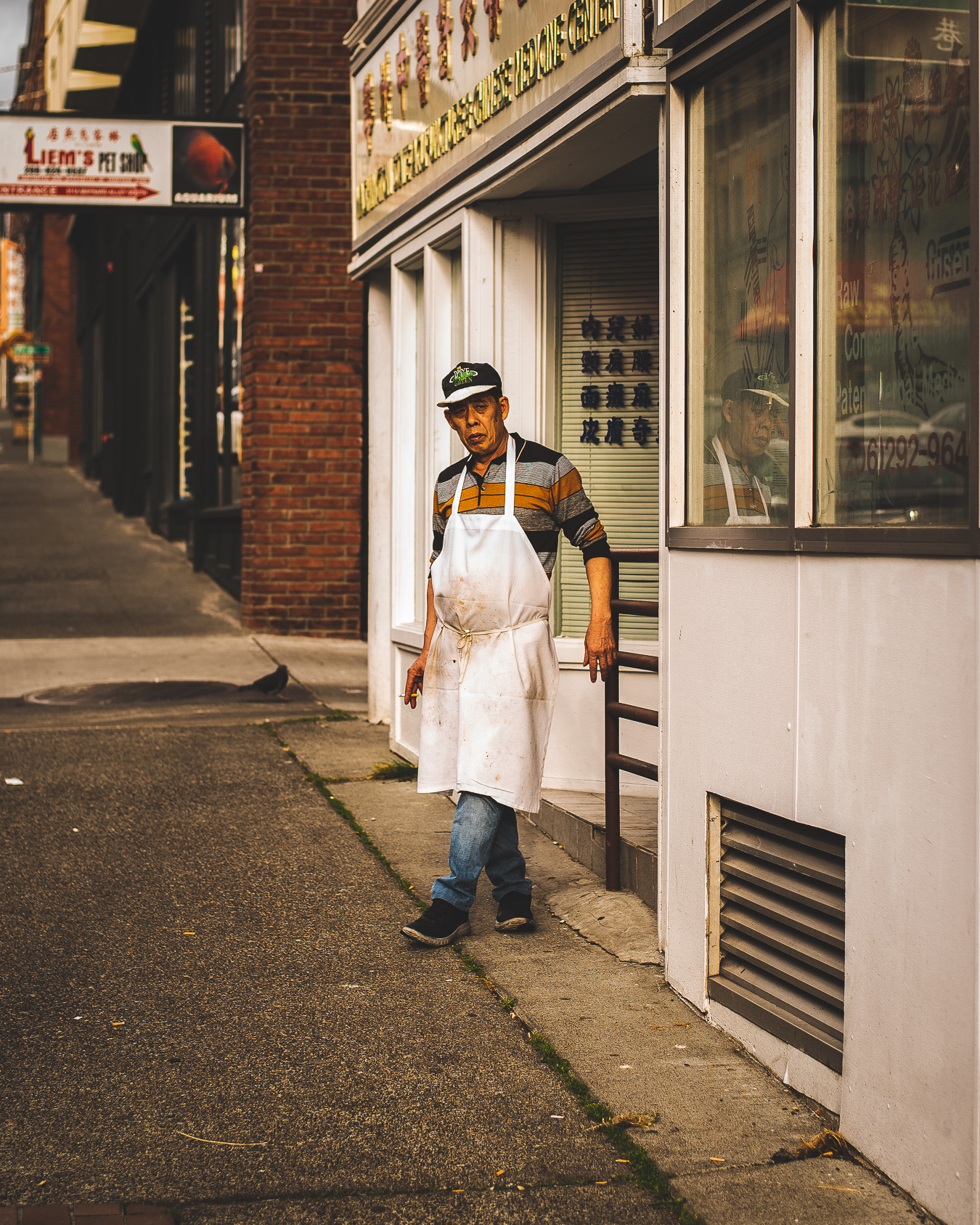 man in apron and cap, standing on sidewalk and smoking a cigarette  outside a Chinese restaurant