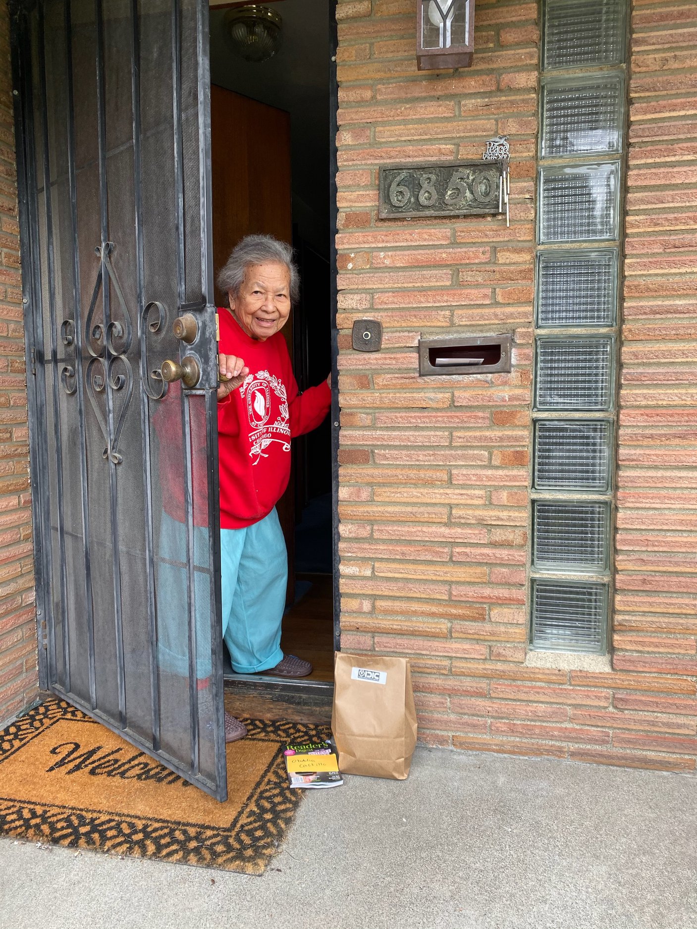 elderly woman smiling and opening her screen door to find a bagged meal on her doorstep