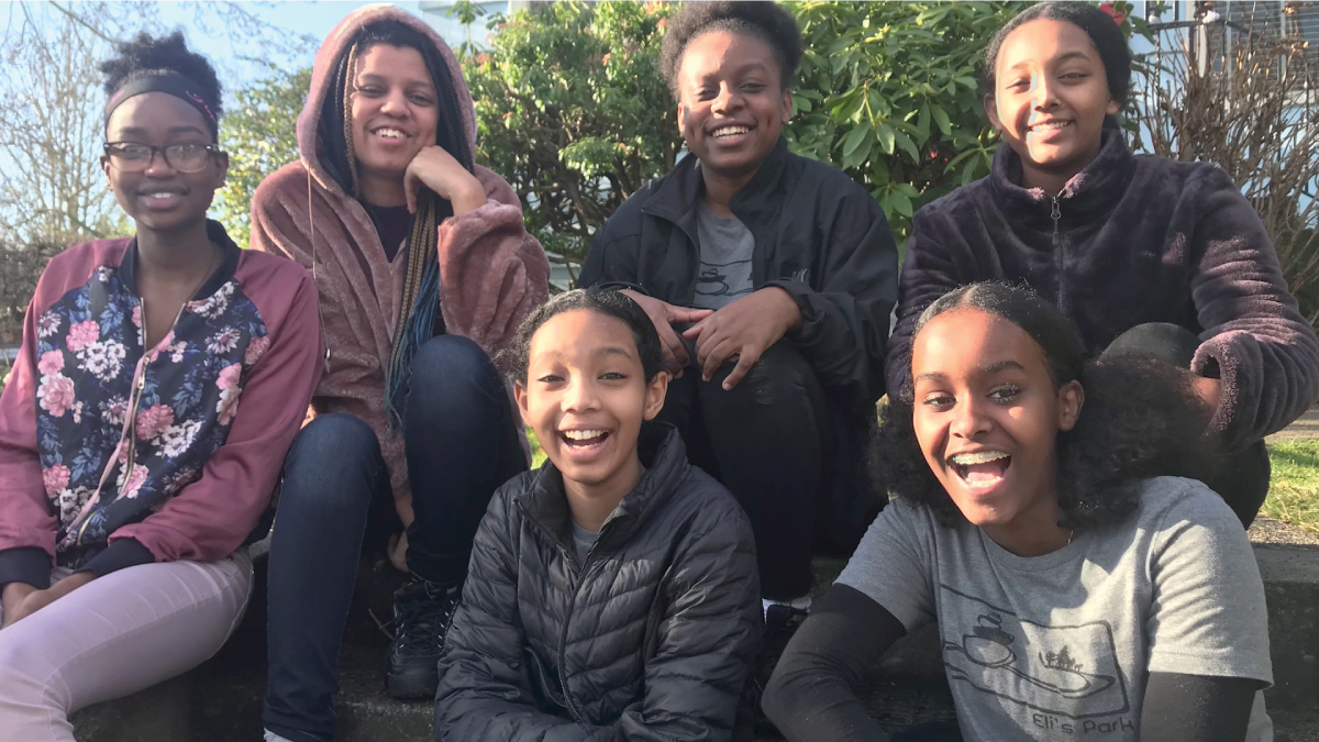 six Black, female teens smiling and sitting outside