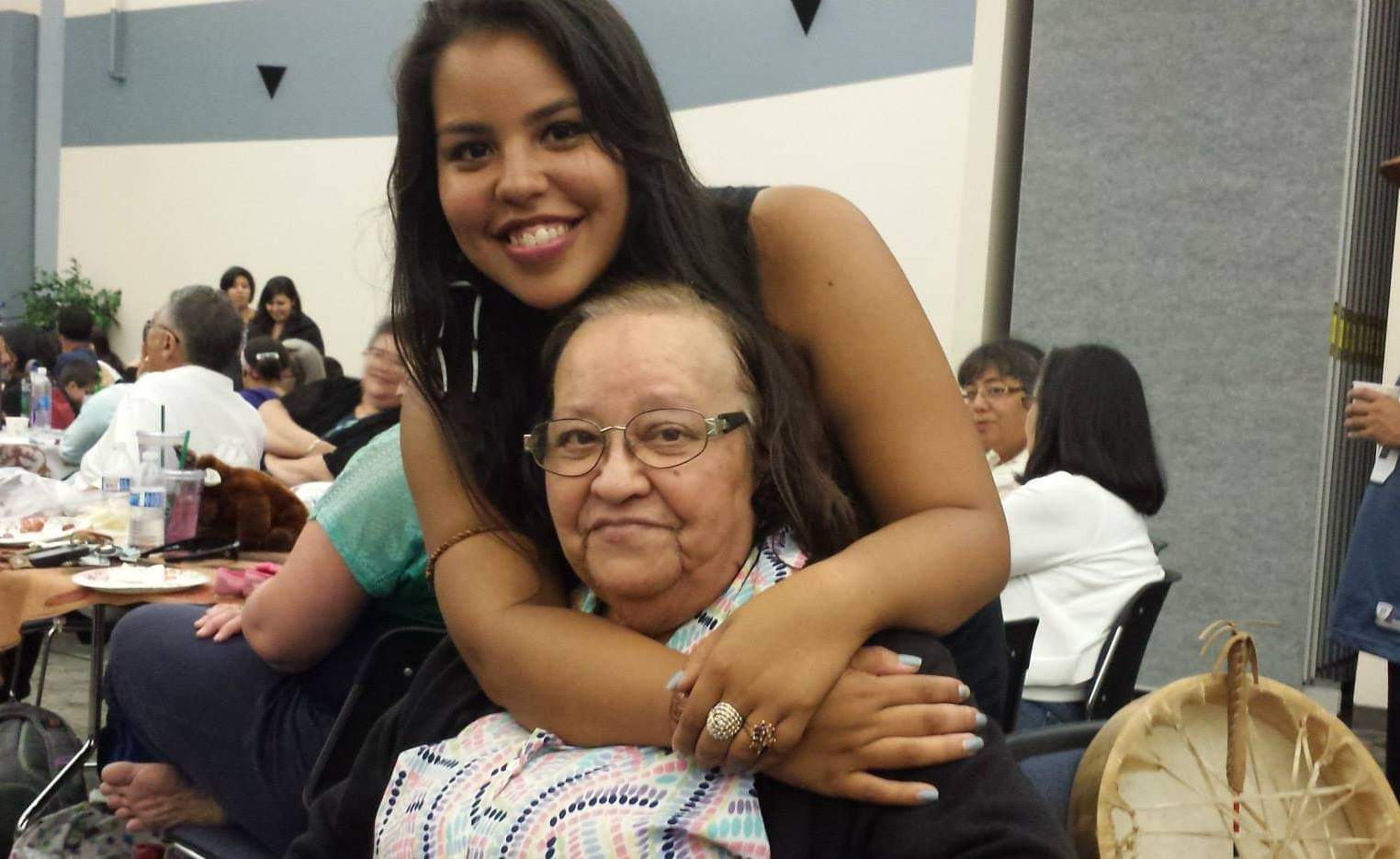 young woman leaning over and embracing older woman.  they are both smiling.