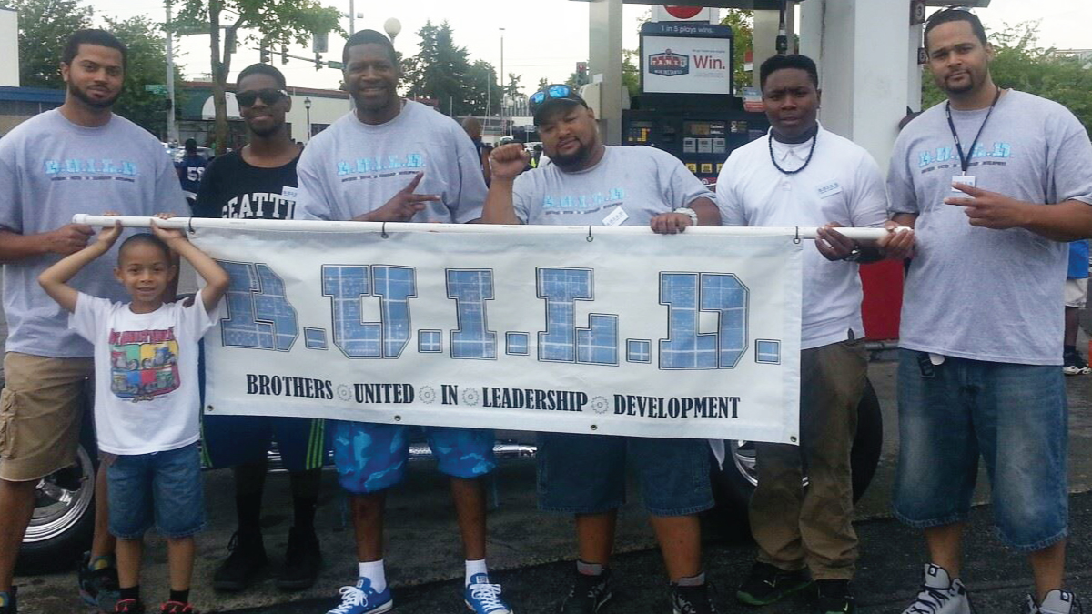 six Black men and one black child, standing outside and holding a banner that reads 