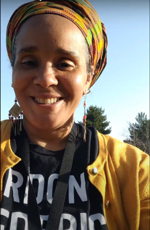 close-up of person in head scarf, standing outside and smiling