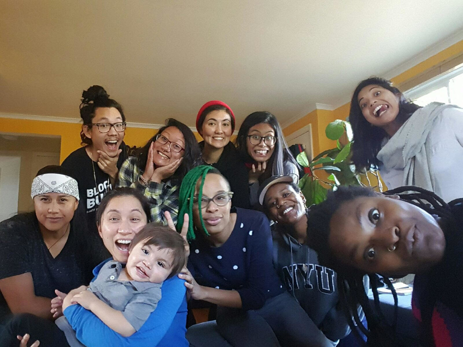group photo of eleven people of color in a house, smiling and laughing