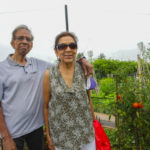 A man, Vasant, has his arm around his wife, Sharda while they stand next to ripening tomato plants in their P-Patch garden plot.