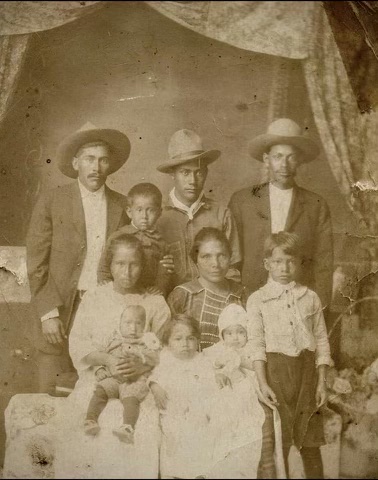 vintage photo of a Mexican family, 3 men in hats standing in back, woman seated center, surrounded by 3 young children and 2 infants