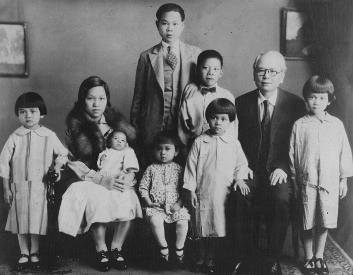 black and white photograph of a Chinese family. There are two adults and seven children of varying ages. They are all dressed formally.