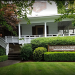 Lush, well-manicured lawn leading up to a bright white, wooden building with covered porch and sign stating, "Hoffner, Fisher and Harvery Funeral Directors"