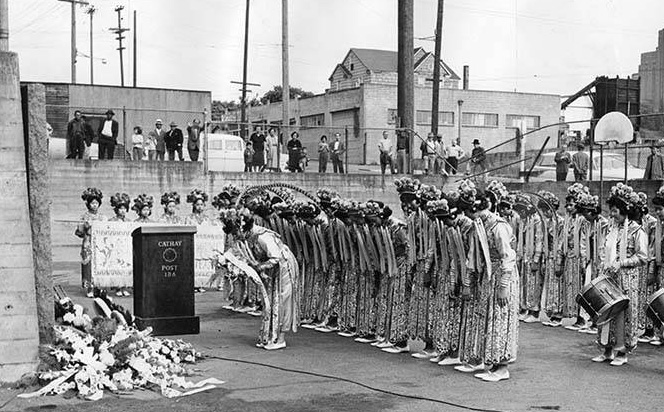 Black and white photo of Drill Team in three-line formation bowing before a podium.