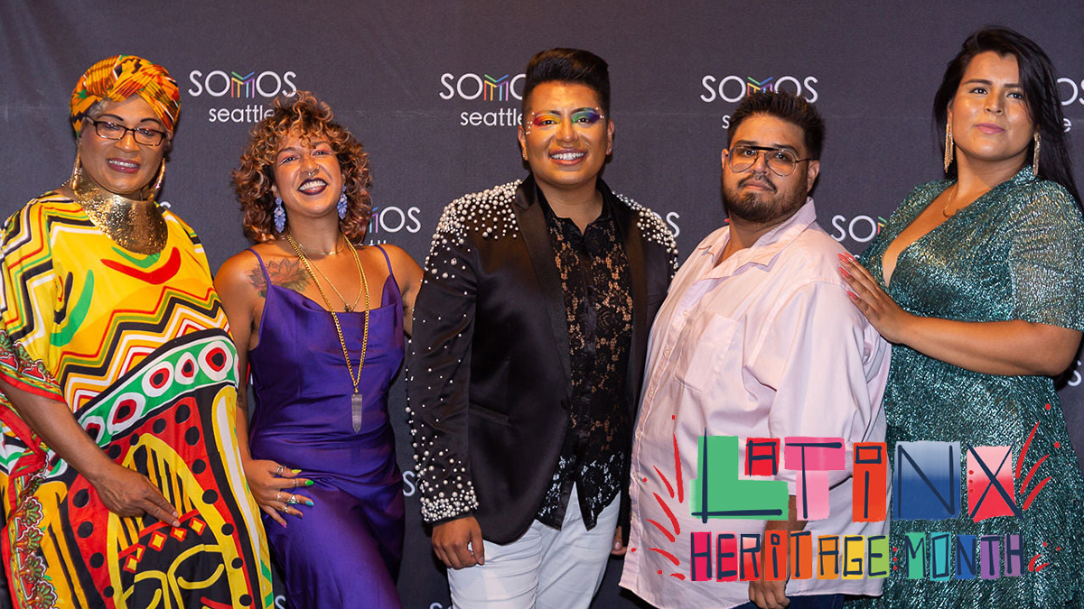 Five people, smiling, and dressed for a celebratory occasion standing together in front of a black backdrop with the logo for Somos Seattle printed on it.