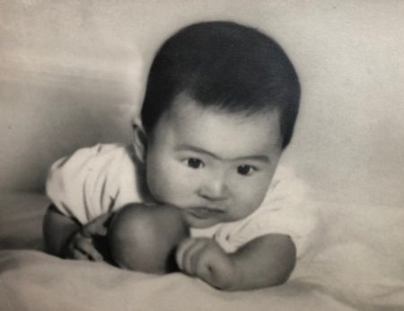 Black and white photo of author as an infant laying on her tummy and looking down with her cheek resting on an apple.