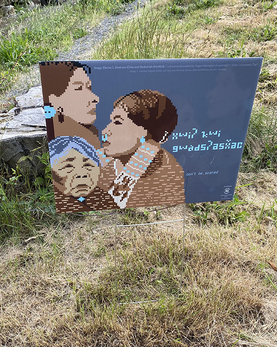 A lawn sign with illustration of three Native peoples and text in an Indigenous language