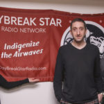 A woman and two men stand in front of a red banner that says "Daybreak Star Radio Network. Indigenize the Airwaves"