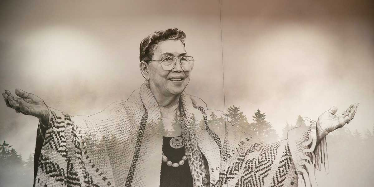 Illustration of Vi Hilbert, arms outstretched and smiling wearing native beads, a woven shawl and misty evergreens fading out in the background. She looks happy.