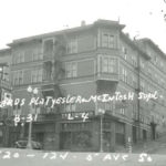 black and white archival photo of a 4-story building with apartments above ground floor storefronts