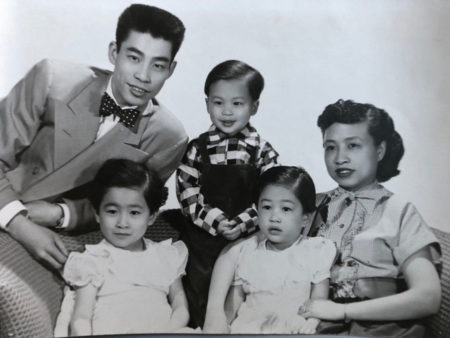 Black and white studio picture of the Lau family with tentative smiles on their faces and dressed in their Easter dresses and and suits and looking their best.