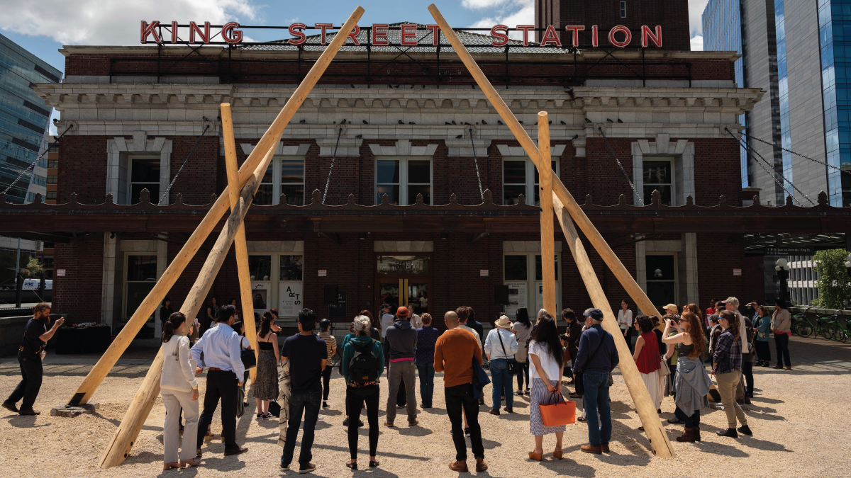 A crowd of people looking at a large art sculpture in front of King Street Station