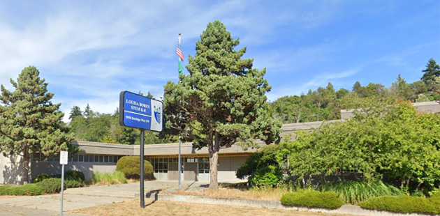 Blue skies and lots of trees surrounding a slightly run down, single-story elementary school with flat roof and a blue sign at the curb that says Louisa Boren STEM K-8