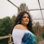 Roxana Pardo Garcia, a Latinx woman with long, curly, dark hair standing on a bridge looking off-camera