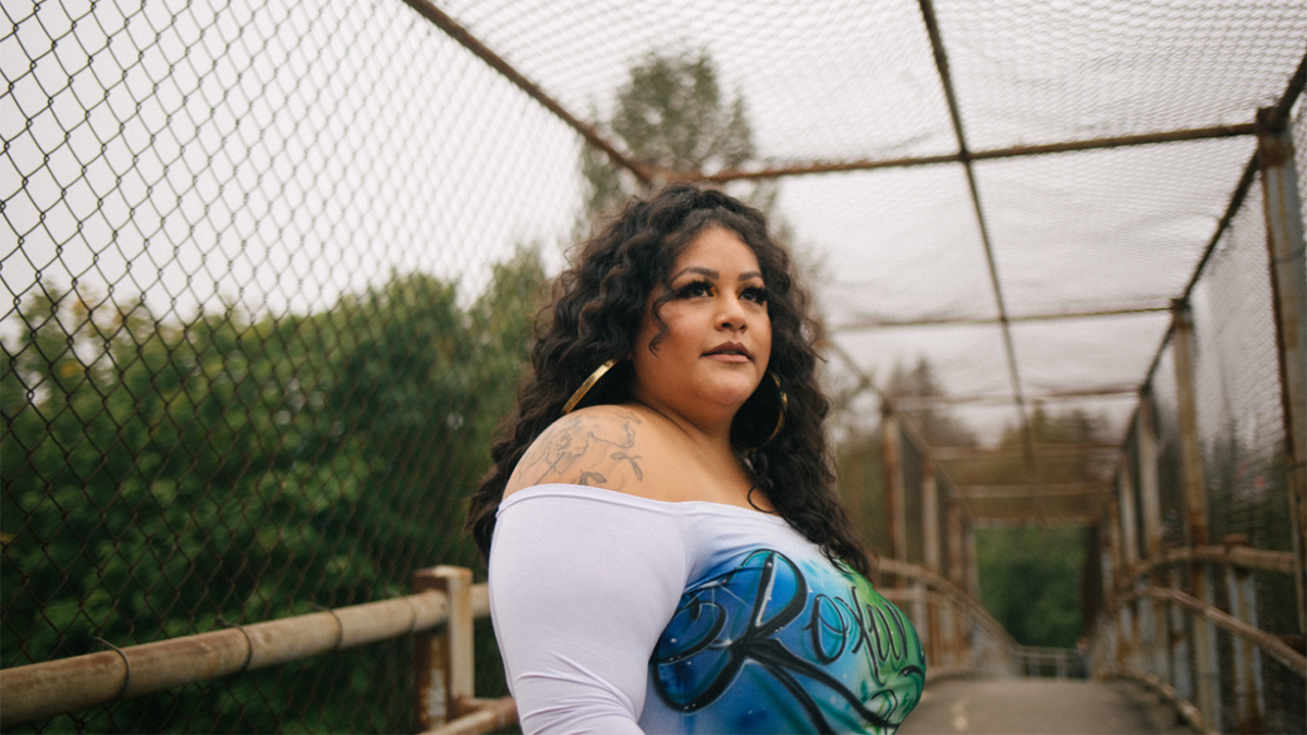 Roxana Pardo Garcia, a Latinx woman with long, curly, dark hair standing on a bridge looking off-camera