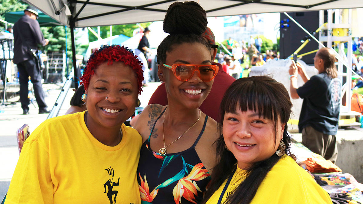 3 smiling people, posing for a photo at an outdoor festival