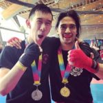 Two martial arts athletes wearing medals smiling and giving a thumbs up sign