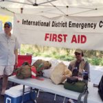 A person standing next to a table with first aid equipment and a sign that says "International District Emergency Center First Aid"