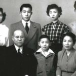 A black and white photo of the Ichikawa family dressed in their best clothes and looking serious, circa 1955