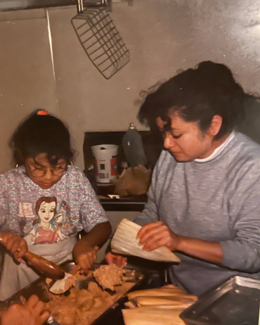 a young girl making tamales with her mother