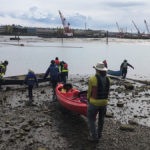 people carrying kayaks into the Duwamish River on a cloudy day