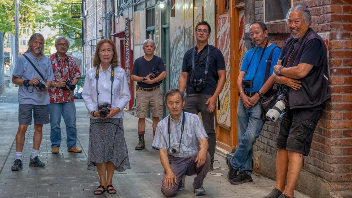 A group of photographers holding cameras stand in an alley in Seattle's Chinatown International District