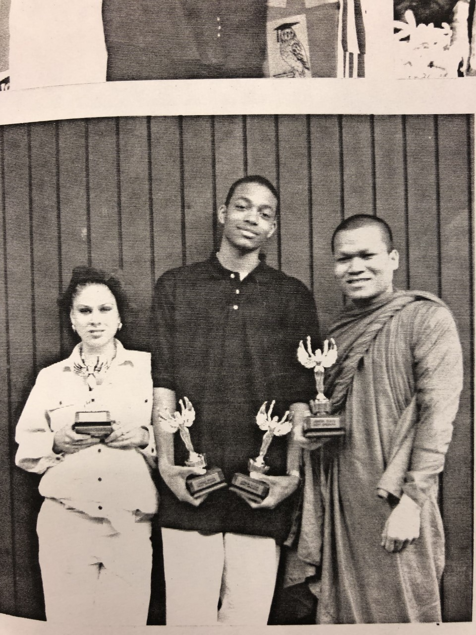 A black and white photo of three teens holding trophies. 