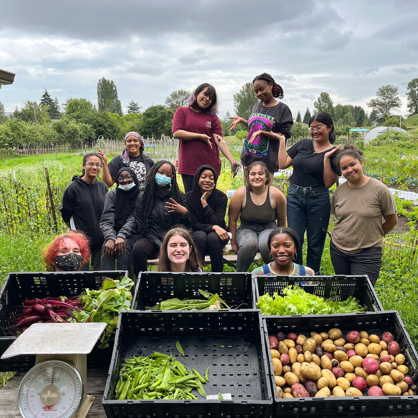 racially diverse group of youth standing in a farm, posing behind a harvest of vegetables