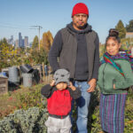 A father and mother stand in the Beacon Food Forest community garden with their three children with the Seattle skyline in the background. The family is of Mam decent, a subgroup of the Mayan nation, who are considered by some to be the best farmers in Guatemala and Mexico.