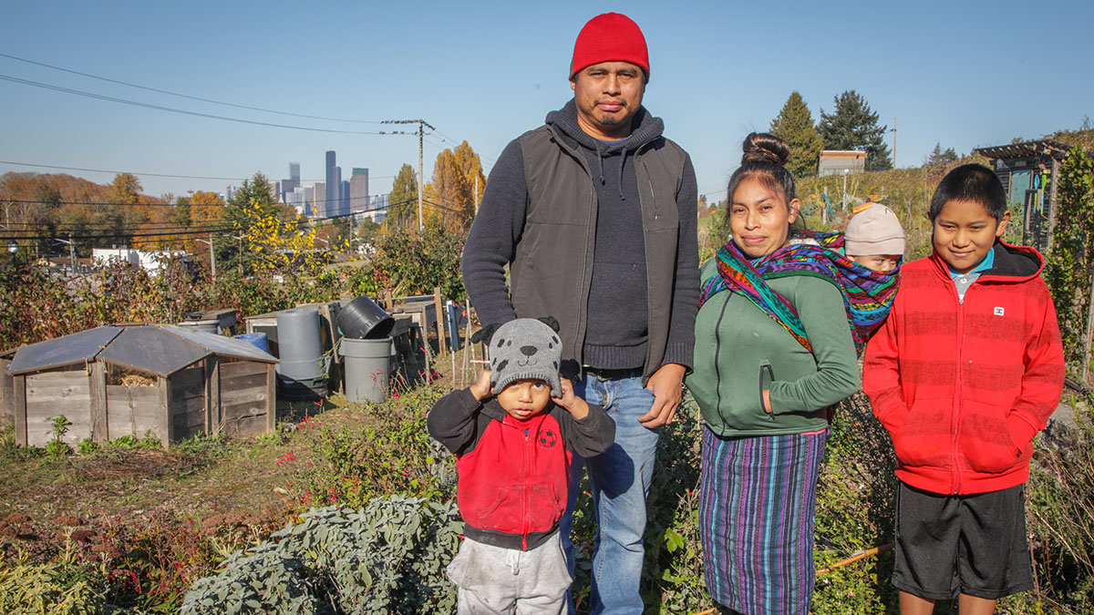 A father and mother stand in the Beacon Food Forest community garden with their three children with the Seattle skyline in the background. The family is of Mam decent, a subgroup of the Mayan nation, who are considered by some to be the best farmers in Guatemala and Mexico.