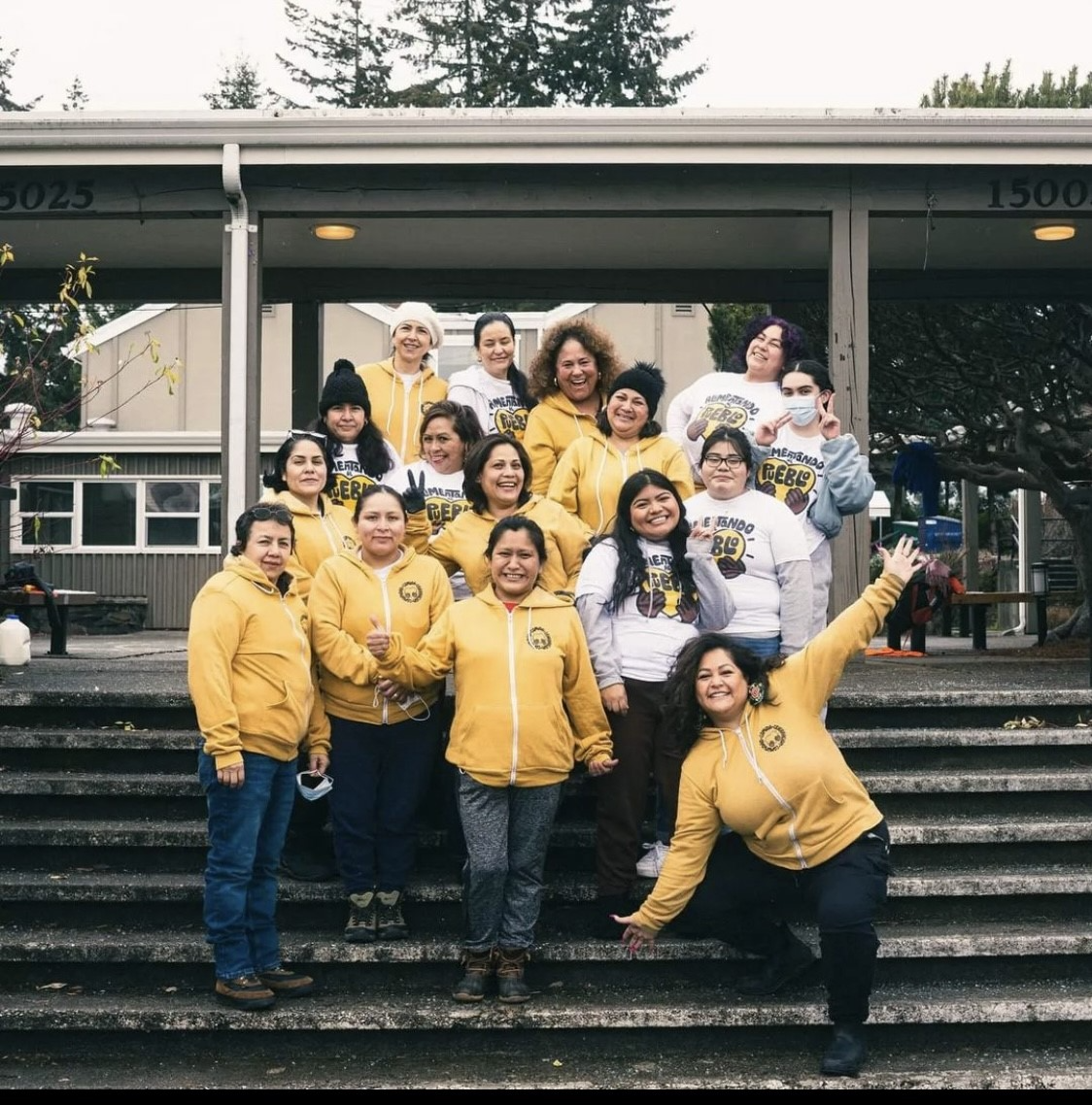 A group of women wearing yellow sweatshirts stand together on an outdoor stairwell. 