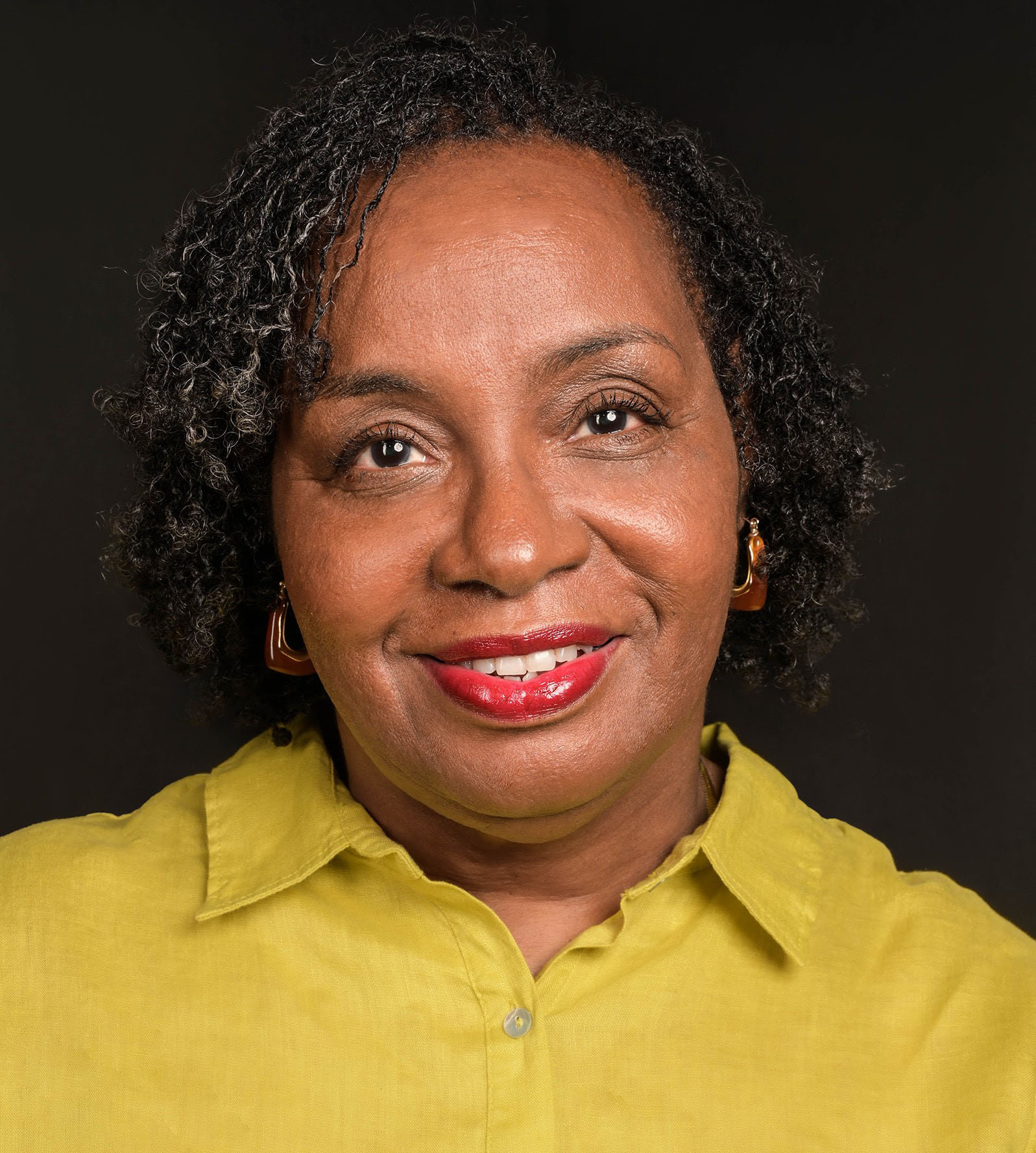 Headshot of a Black woman with red lipstick, gold earrings, and a yellow collard shirt. 