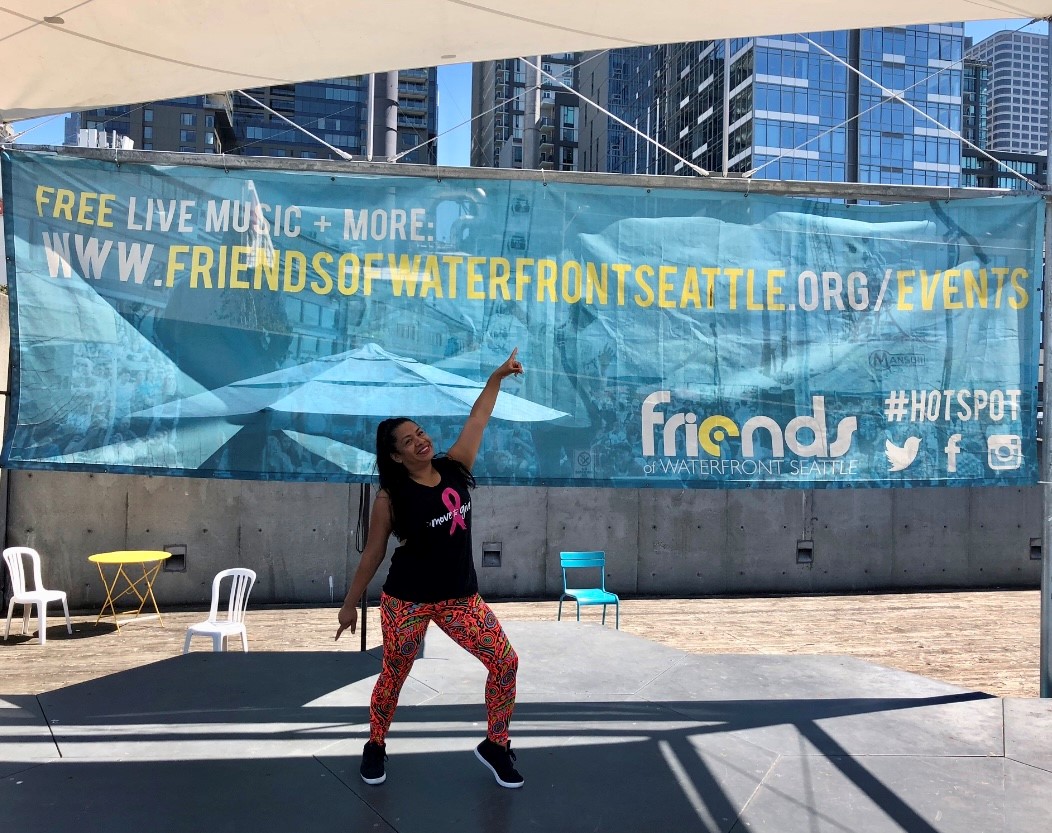 A woman wearing workout clothes posing in front of a large sign that says "Friends of Waterfront Seattle."
