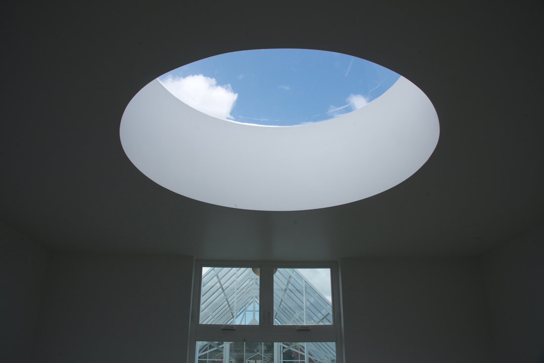 View of a ceiling of a room with a round window looking up to a blue sky with a glass door on the wall below. 