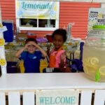 Two kids smiling and being goofy in a lemonade stand.