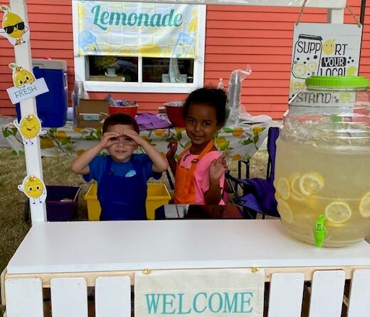 Two kids smiling and being goofy in a lemonade stand.
