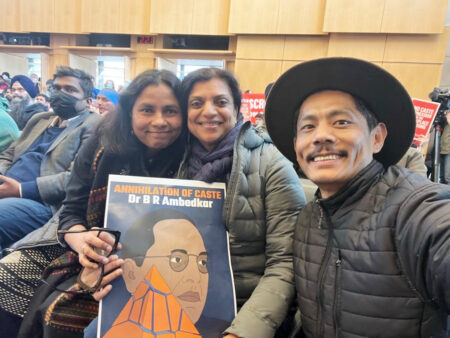image of 2 South Asian women and 1 South Asian man posing for the camera in Seattle City Council chambers. They are holding a poster that reads "Annihilation of Caste"