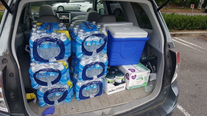 The rear of a hatchback vehicle open and filled with large packages of bottled water and a cooler. 