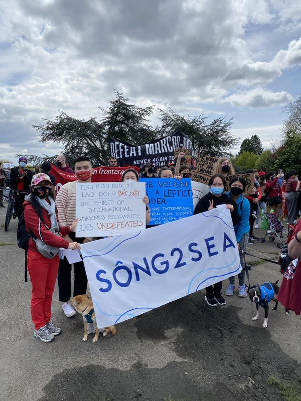 A group of young people wearing health facemasks hold up handwritten signs and a banner that reads "SONG2SEA."