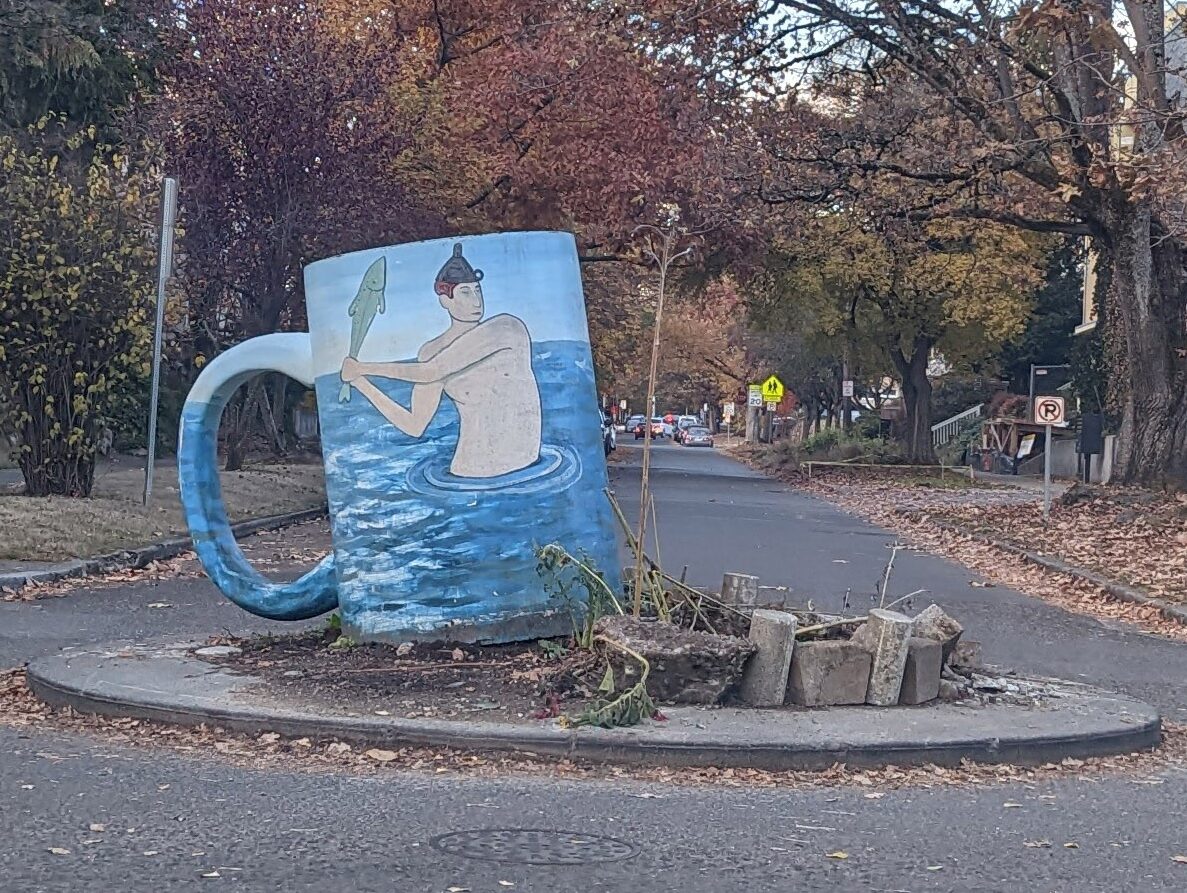 A roundabout at an street intersection with a large artwork sculpture of a coffee mug.