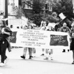 black and white photo of group of people marching in Pride Parade. several people are carrying a banner that reads "The 1993 Seattle Lesbian / Gay / Bisexual / Transgender Pride Parade March and Freedom Rally"