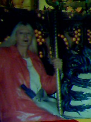 blurry photo of a transgender woman will long blonde hair, wearing a long pink coat and riding a carousel.