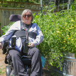 A woman in an electric wheelchair pictured in a garden with a raised trough bed.